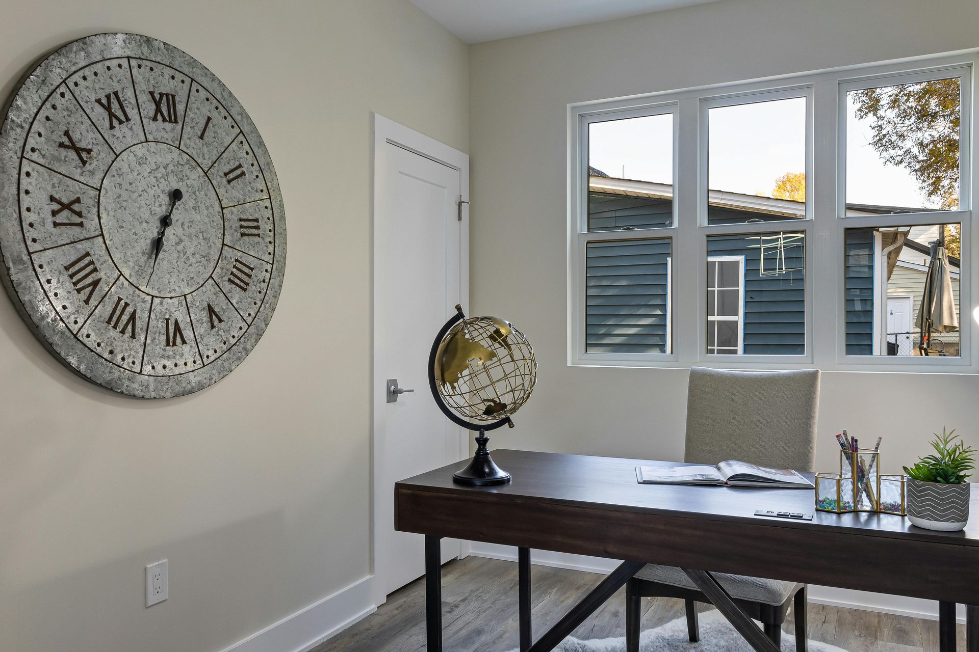 A home office with a large clock on the wall above a desk.