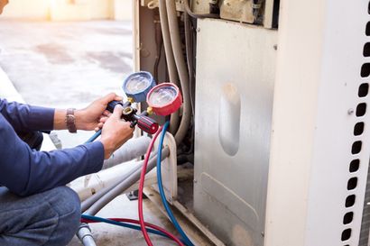 Technician using gauges to inspect HVAC outdoor unit with connected hoses and meters
