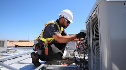 Technician in hard hat servicing rooftop HVAC equipment next to a large unit.