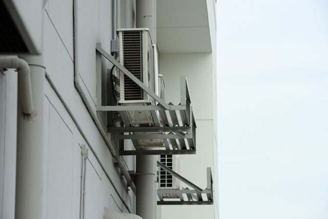 Row of metal air-conditioning units mounted on a gray building wall against a pale sky