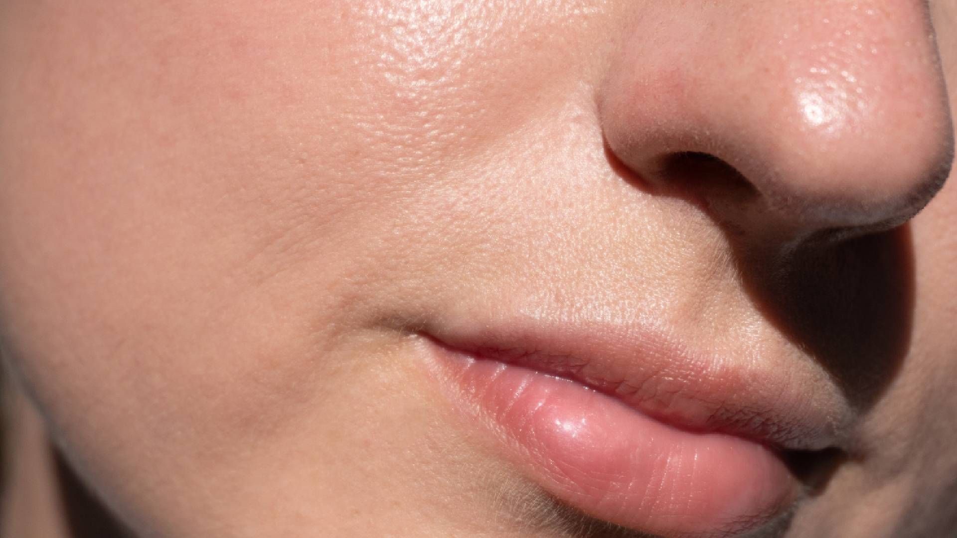 Close-up of a person's face showing skin texture, nose, and lips. The skin appears shiny, possibly with makeup.