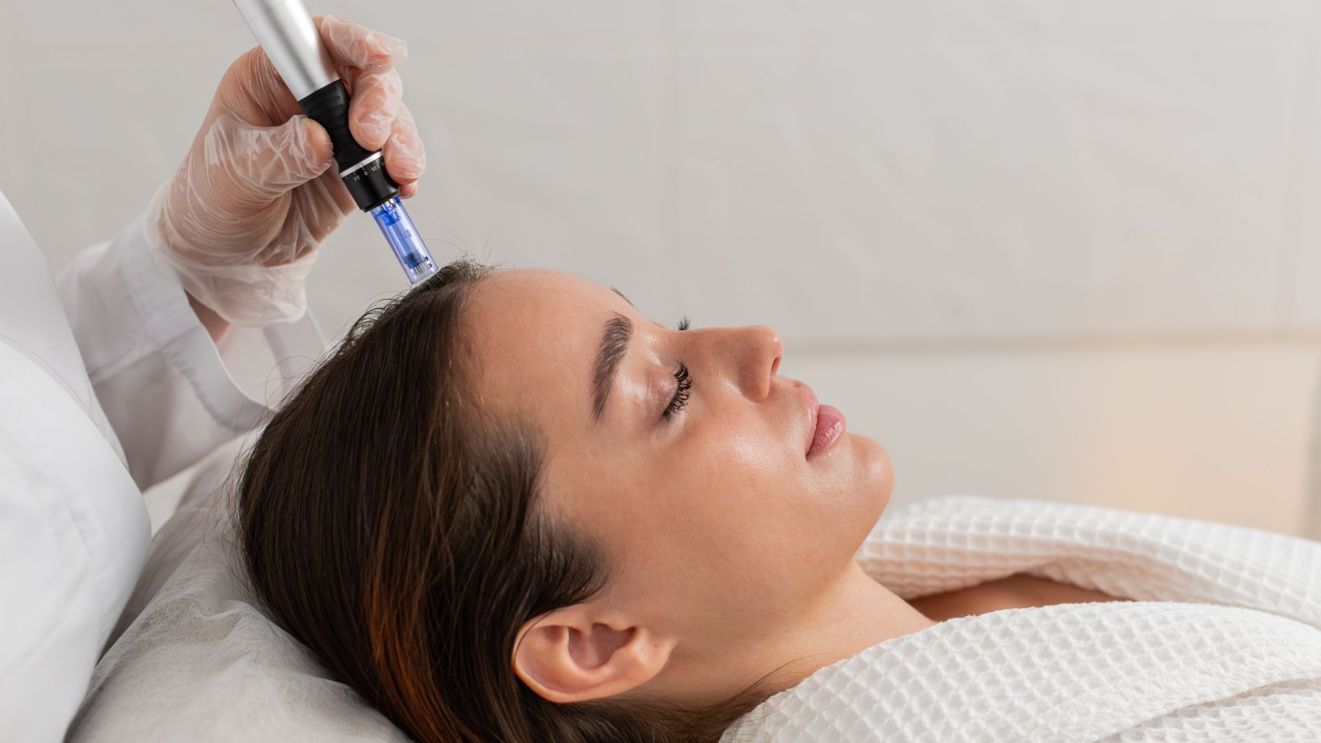 A person receives a scalp microneedling treatment from a professional in a clinical setting.