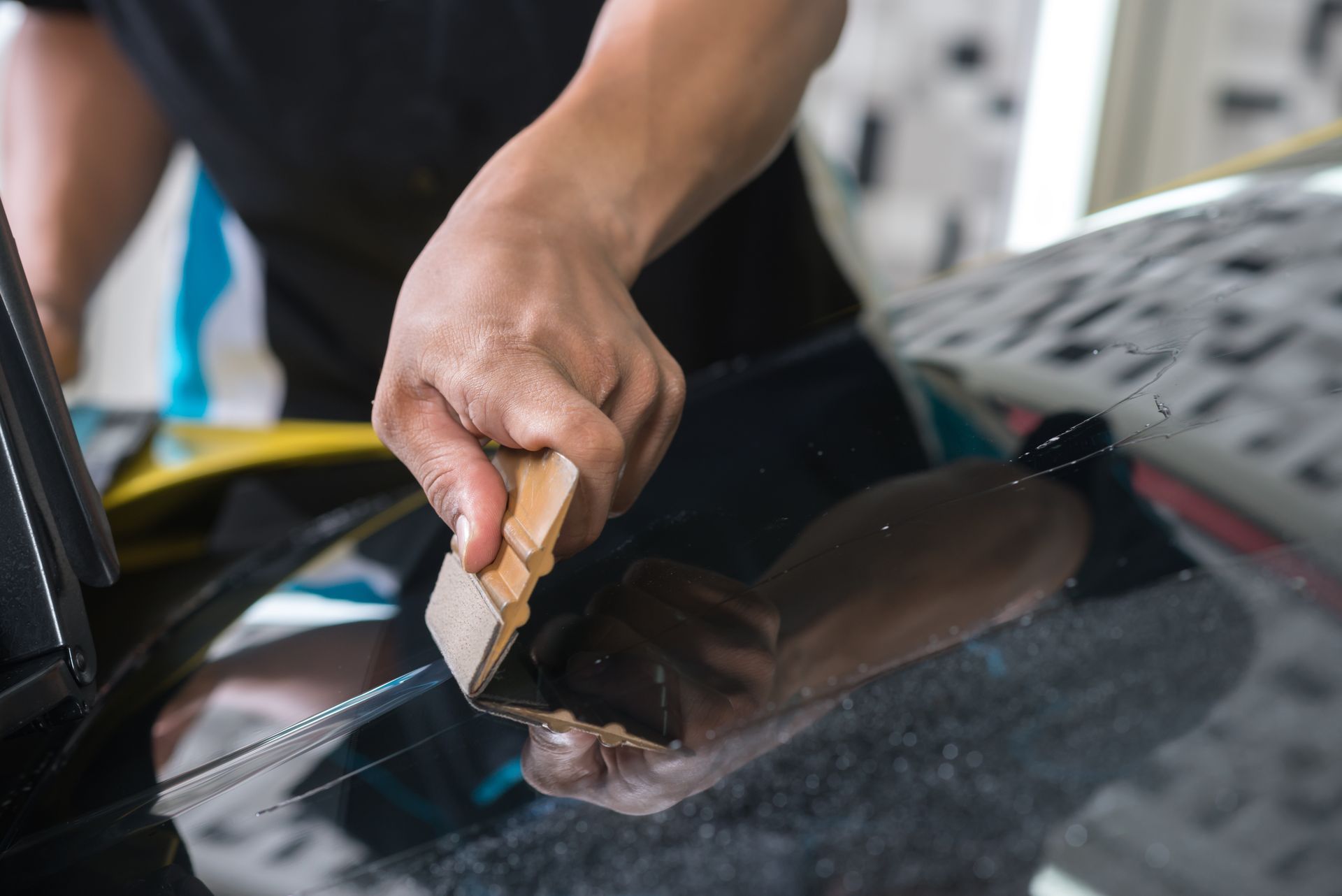 Person using a squeegee to apply tint to a car window.