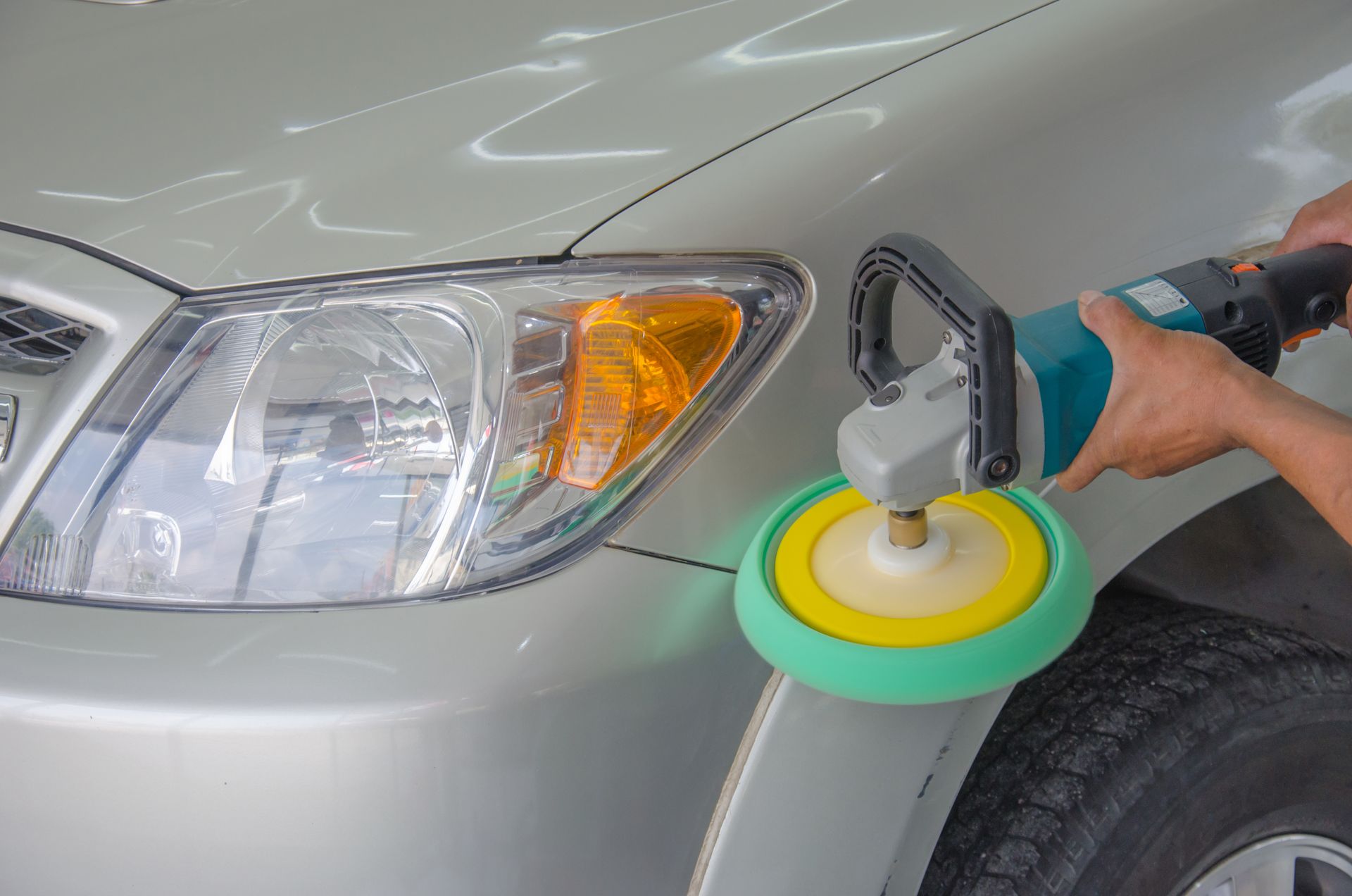 Person polishing car's body with an electric buffer near the headlight.