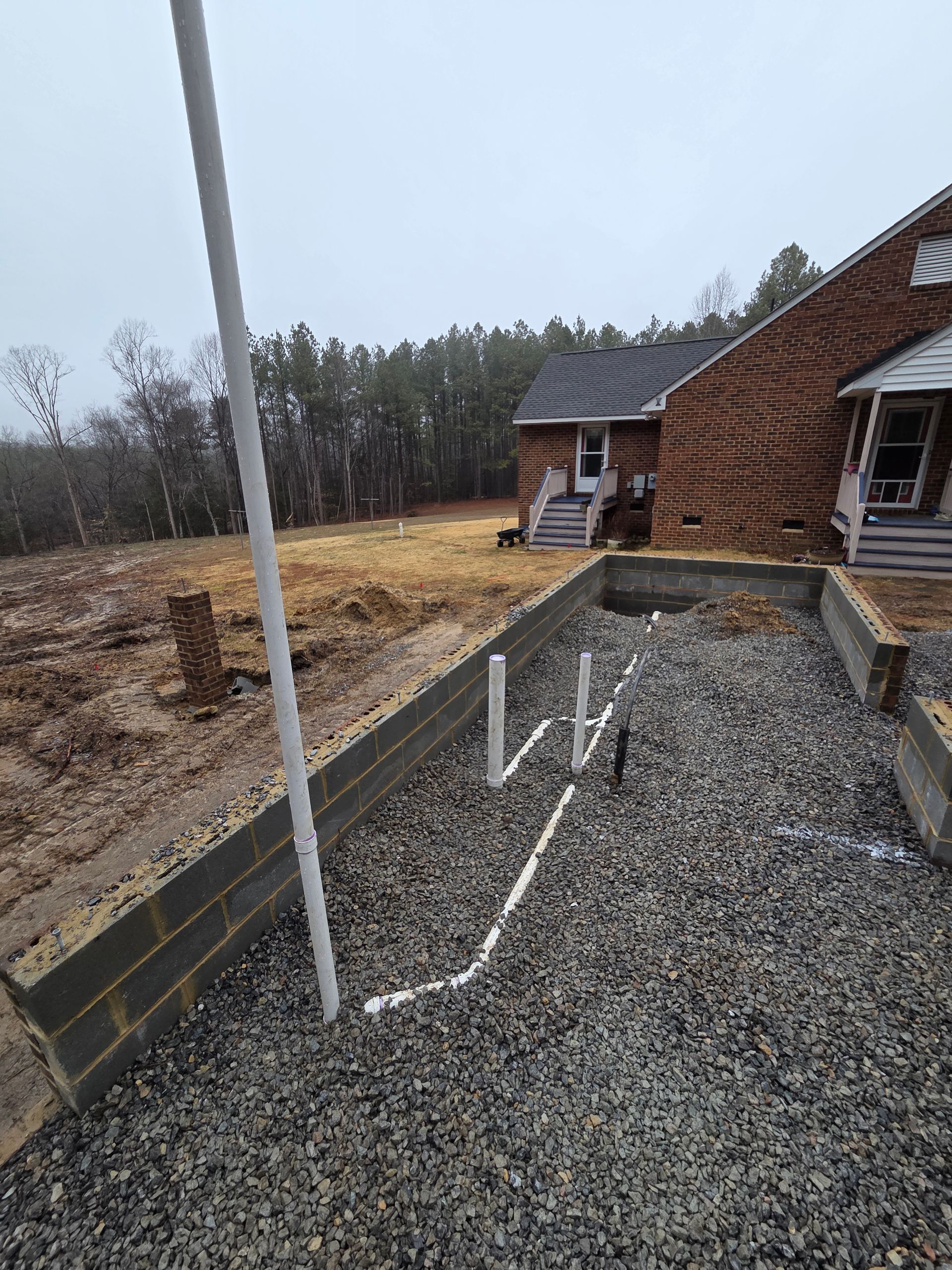 Gravel walkway with white handrails leading to a house entrance beside a wooded yard.