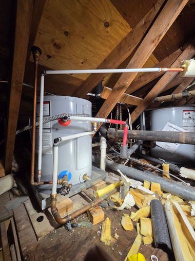 Attic with exposed insulation and two water heaters among pipes and debris