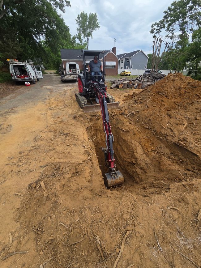 Excavator digging a trench in a muddy residential construction site with houses in the background