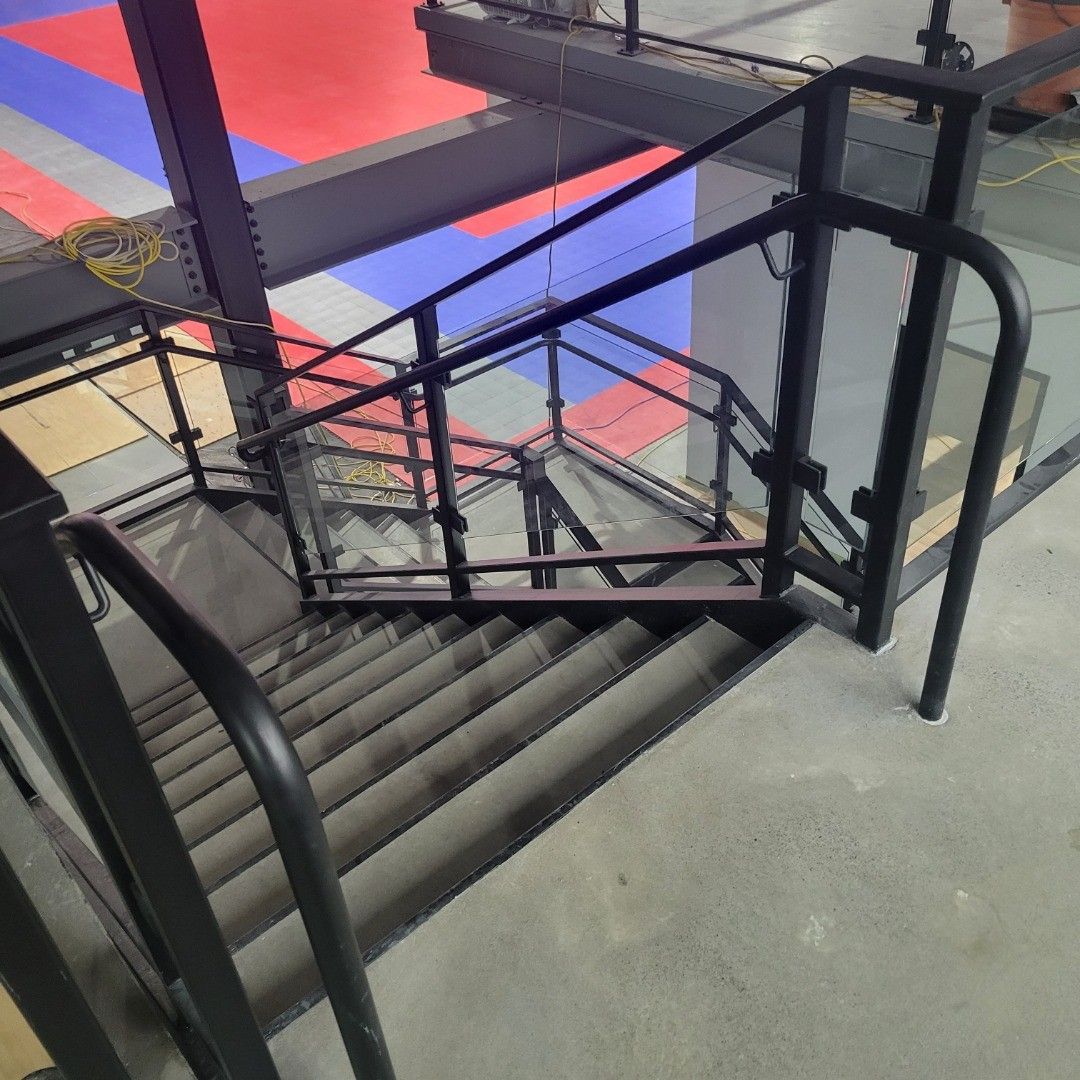 Staircase with black metal handrails and concrete steps, leading up to a platform.