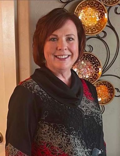 A woman is smiling in front of a wall with plates on it.