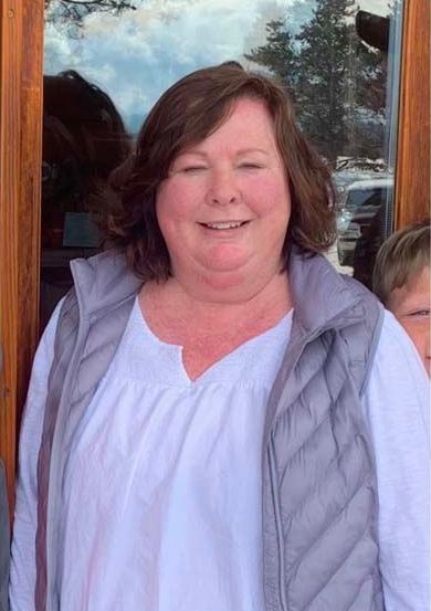 A woman wearing a gray vest and a white shirt is smiling.