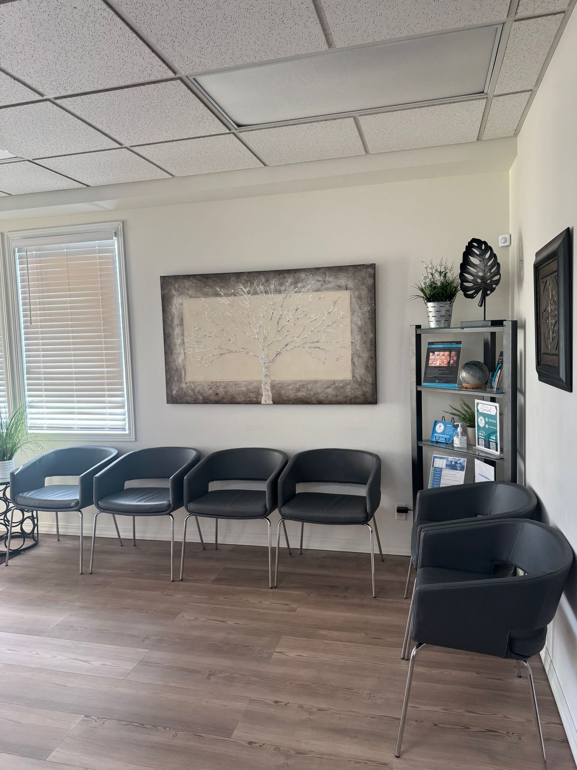 Waiting room with black chairs, framed wall art, and a shelving unit in a bright office.