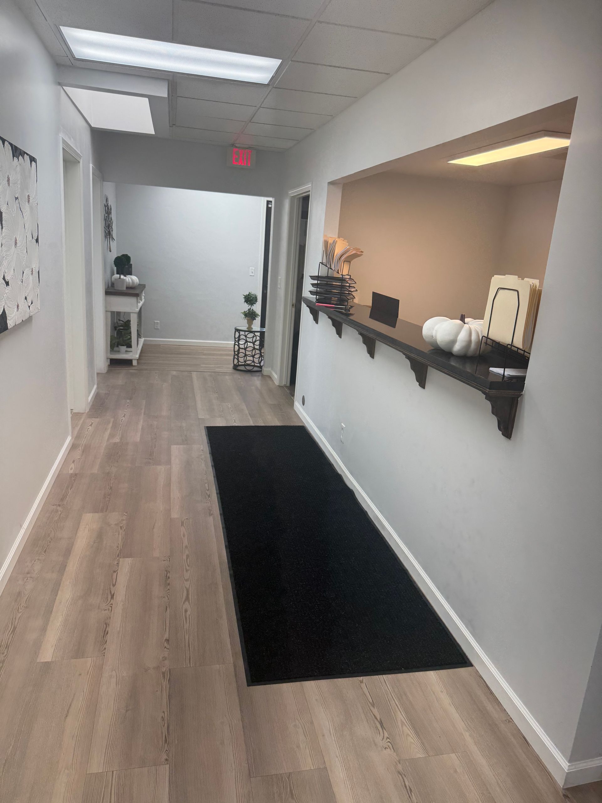 Indoor office hallway with reception counter, light wood floors, white walls, and a dark floor runner.