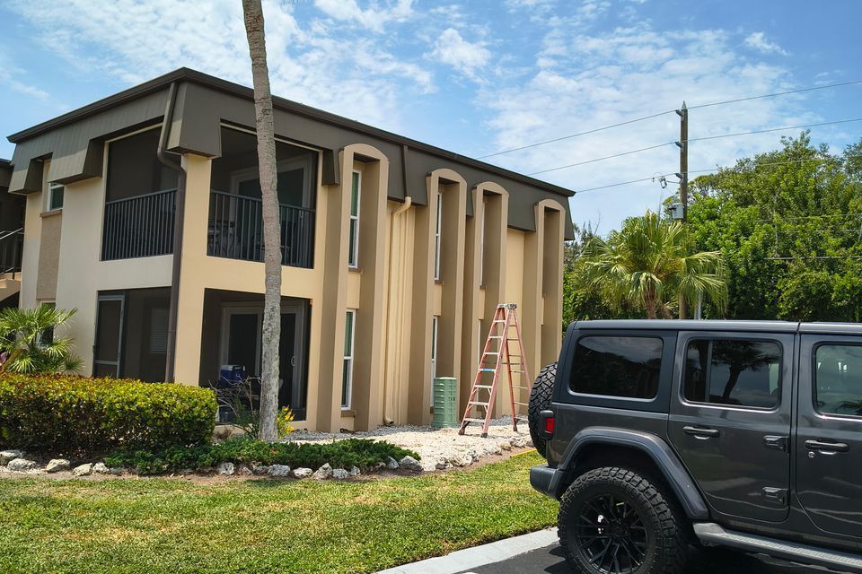 Two-story beige house with dark trim, a ladder by the entrance, and a parked black SUV in front.