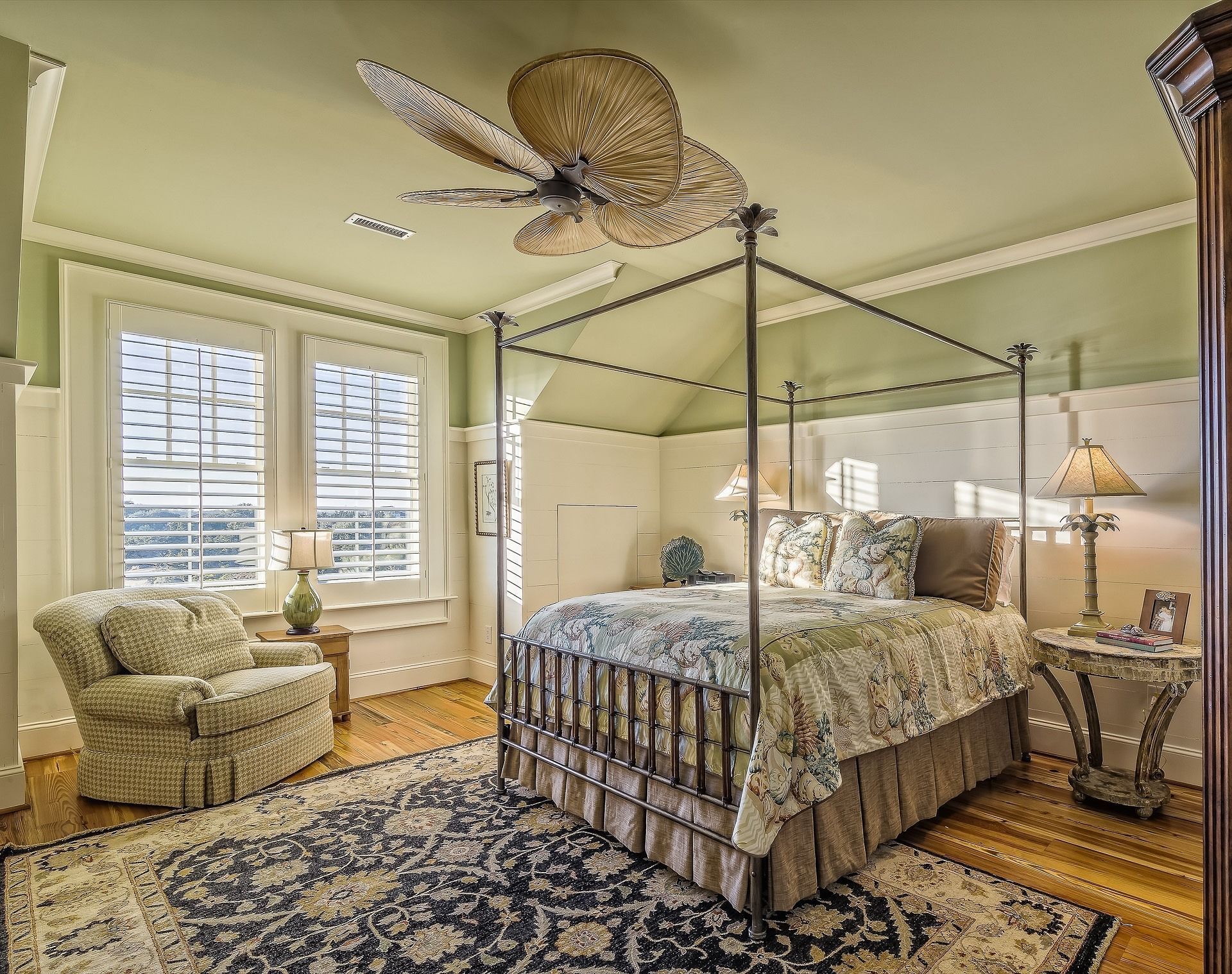 Elegant bedroom with a canopy bed, floral armchair, patterned rug, and large windows with shutters