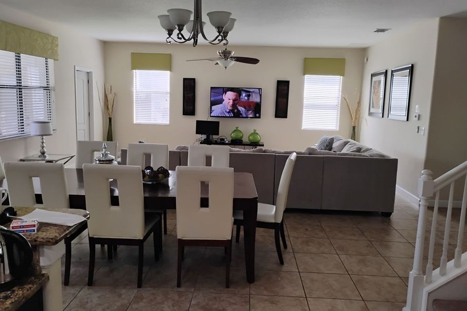 Open-plan living and dining room with tiled floor, gray sofa, dining table, and TV on the wall