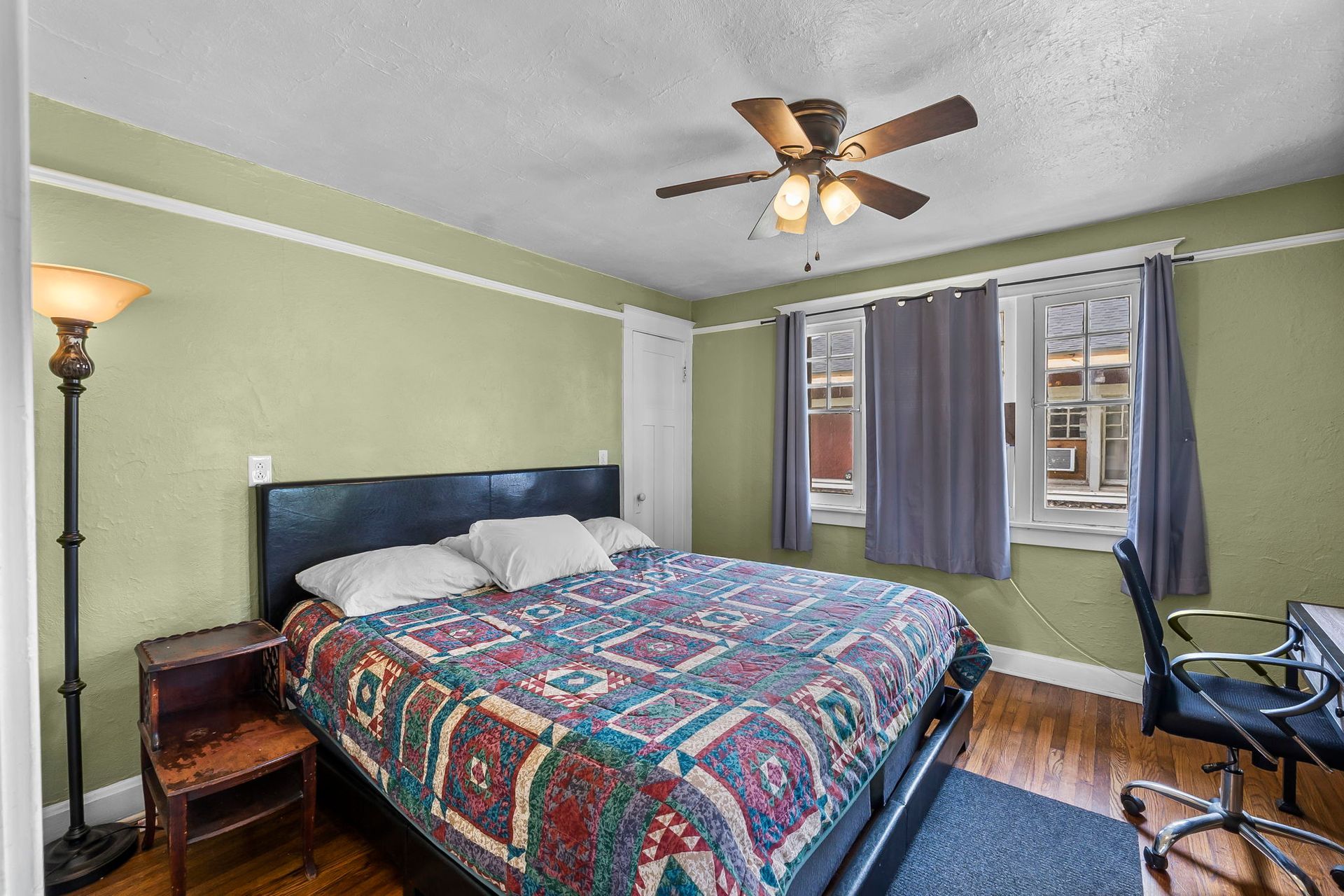 a bedroom with a bed , desk , lamp and ceiling fan .