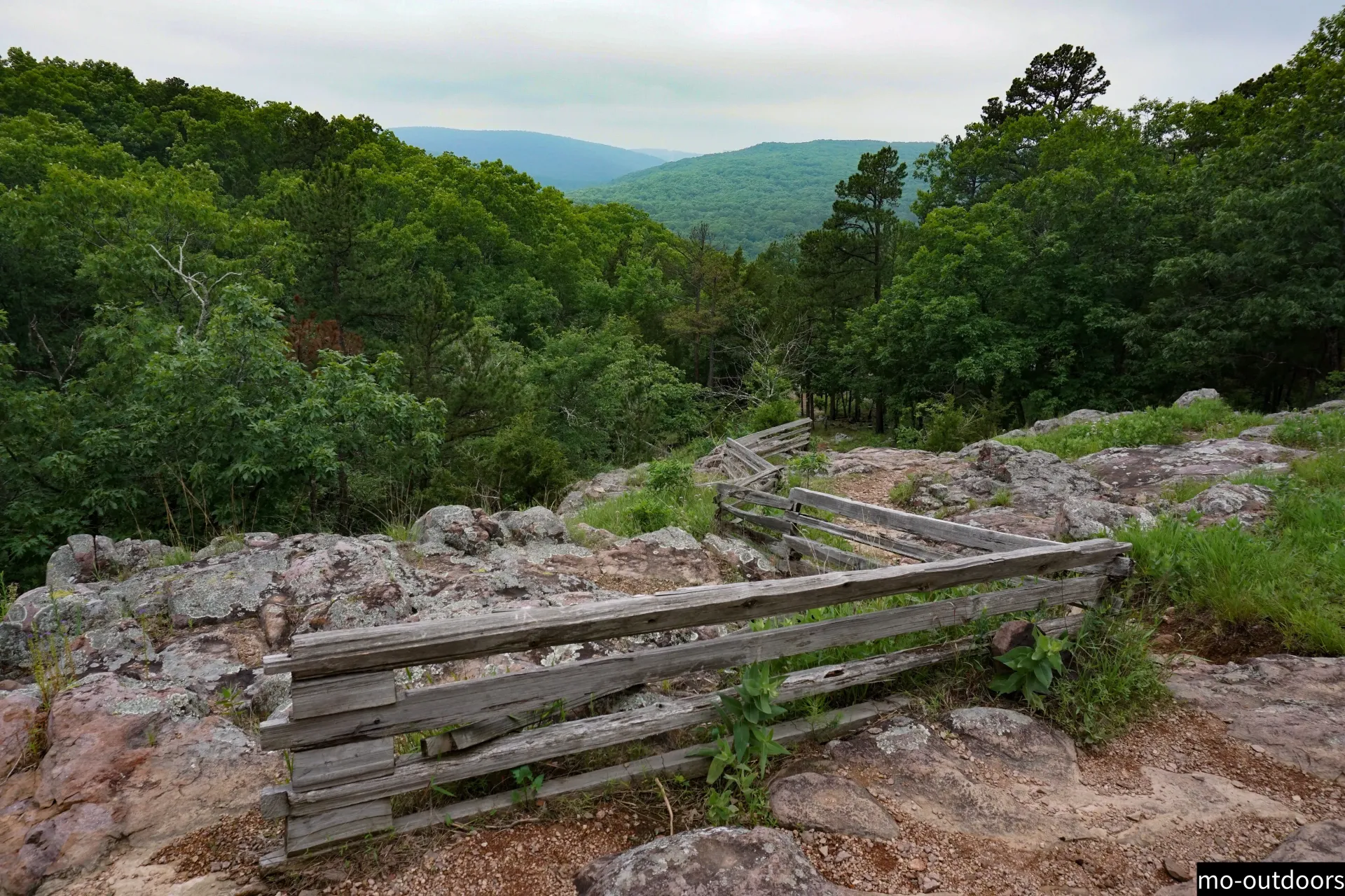 A wooden fence is sitting on top of a rocky hill with trees in the background.