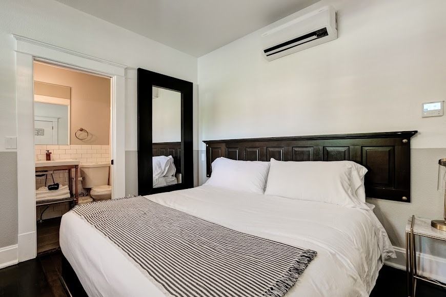 Bright bedroom with a white bed, dark wood headboard, mirrored closet, and bathroom doorway