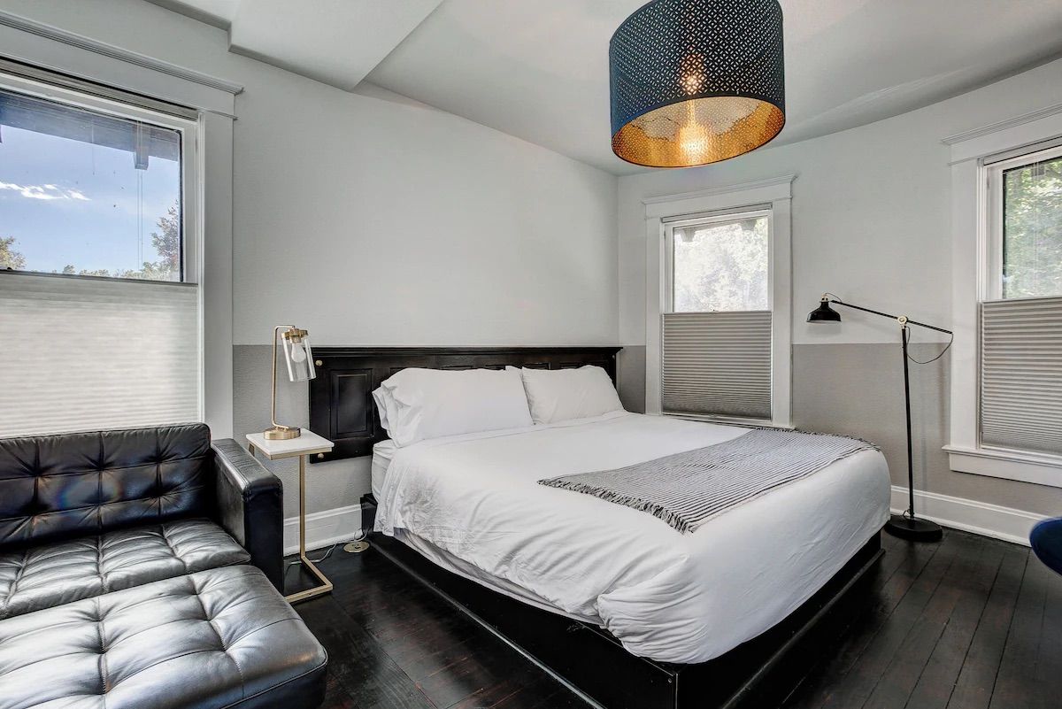 Modern bedroom with black bed, tufted sofa, white walls, and windows with shades