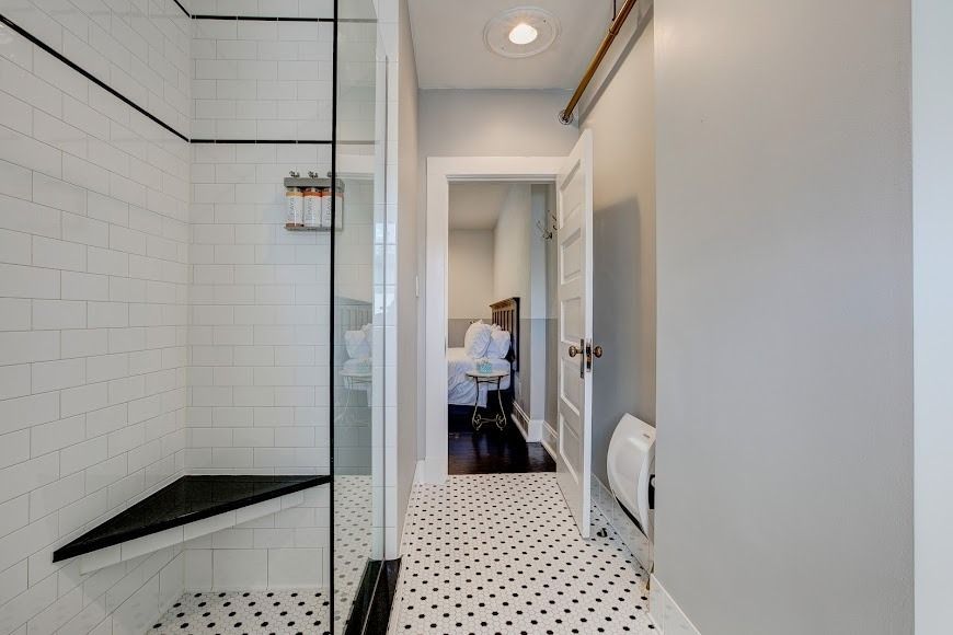 Narrow bathroom hallway with black-and-white tile, glass shower on left, and toilet at the end.