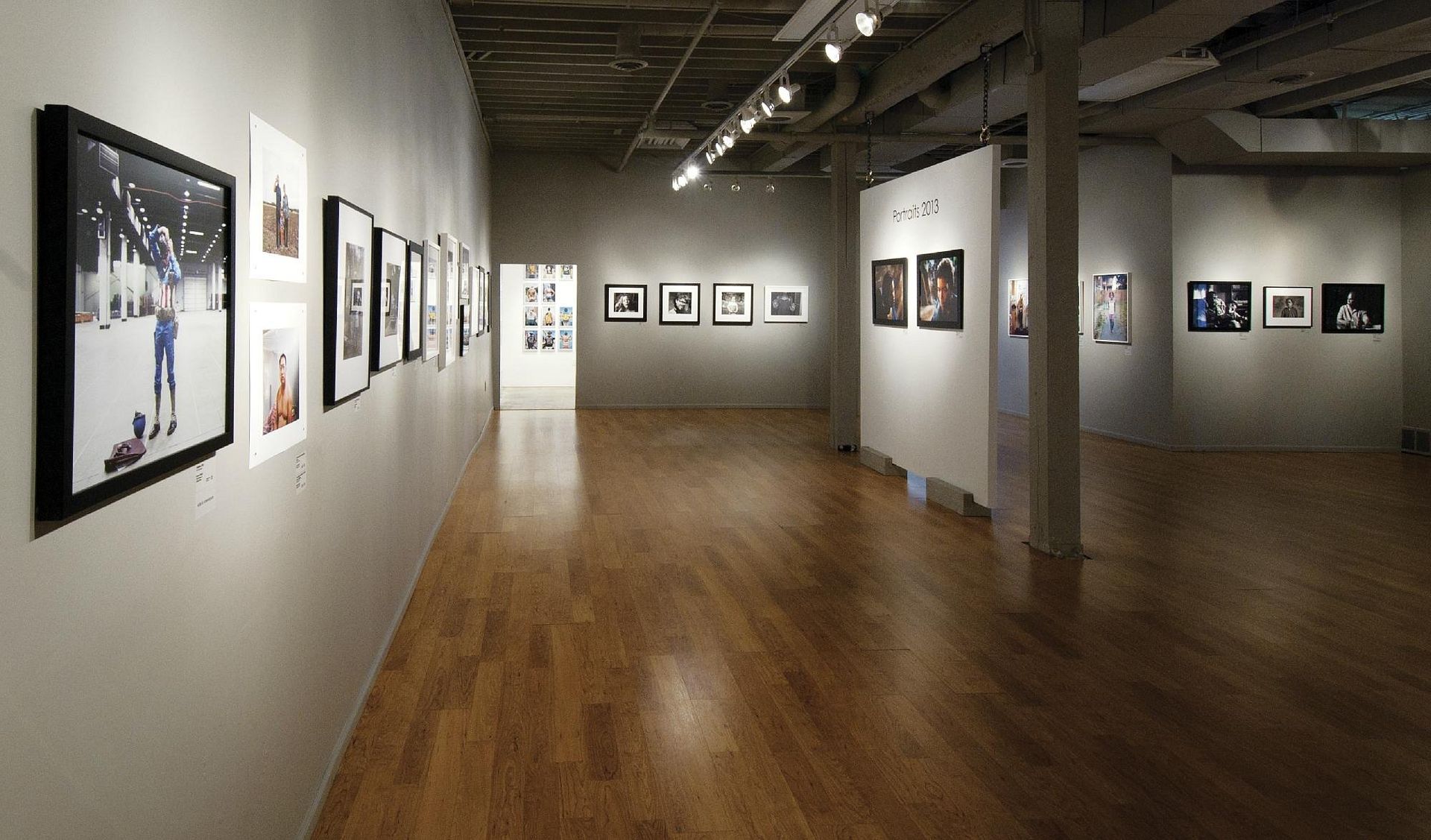 Art gallery hallway with framed black-and-white photos on white walls and a polished wooden floor