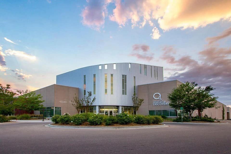 Modern building exterior with curved silver facade, trees, and a sunset sky