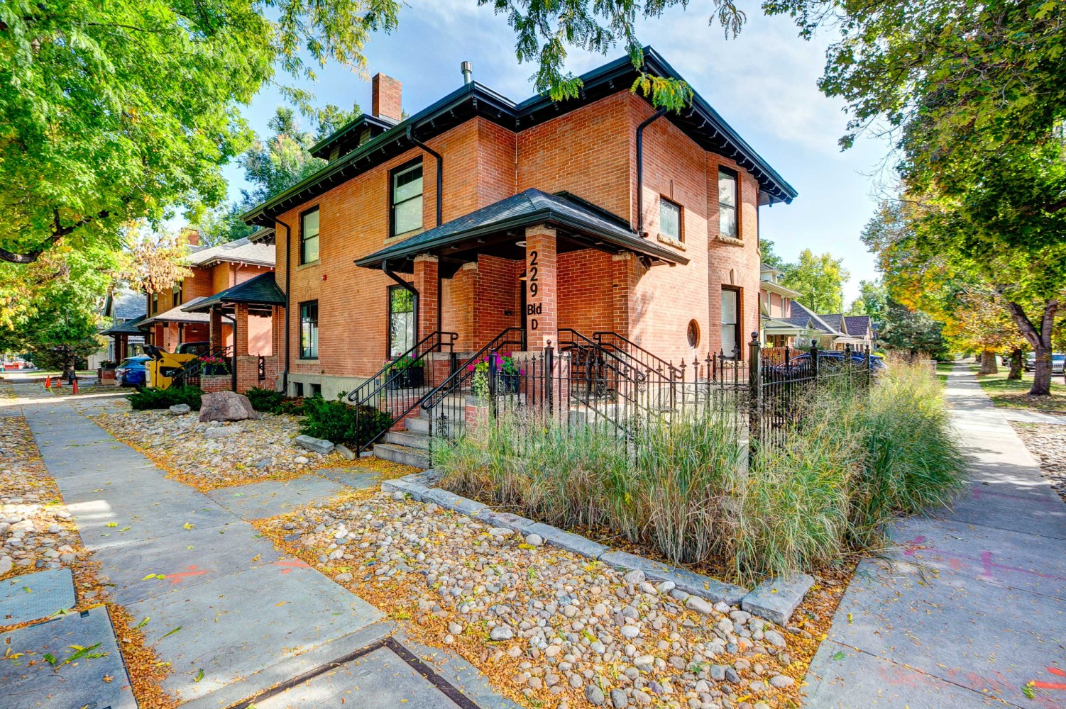 Brick house on a tree-lined corner with yellow leaves and sidewalks in autumn