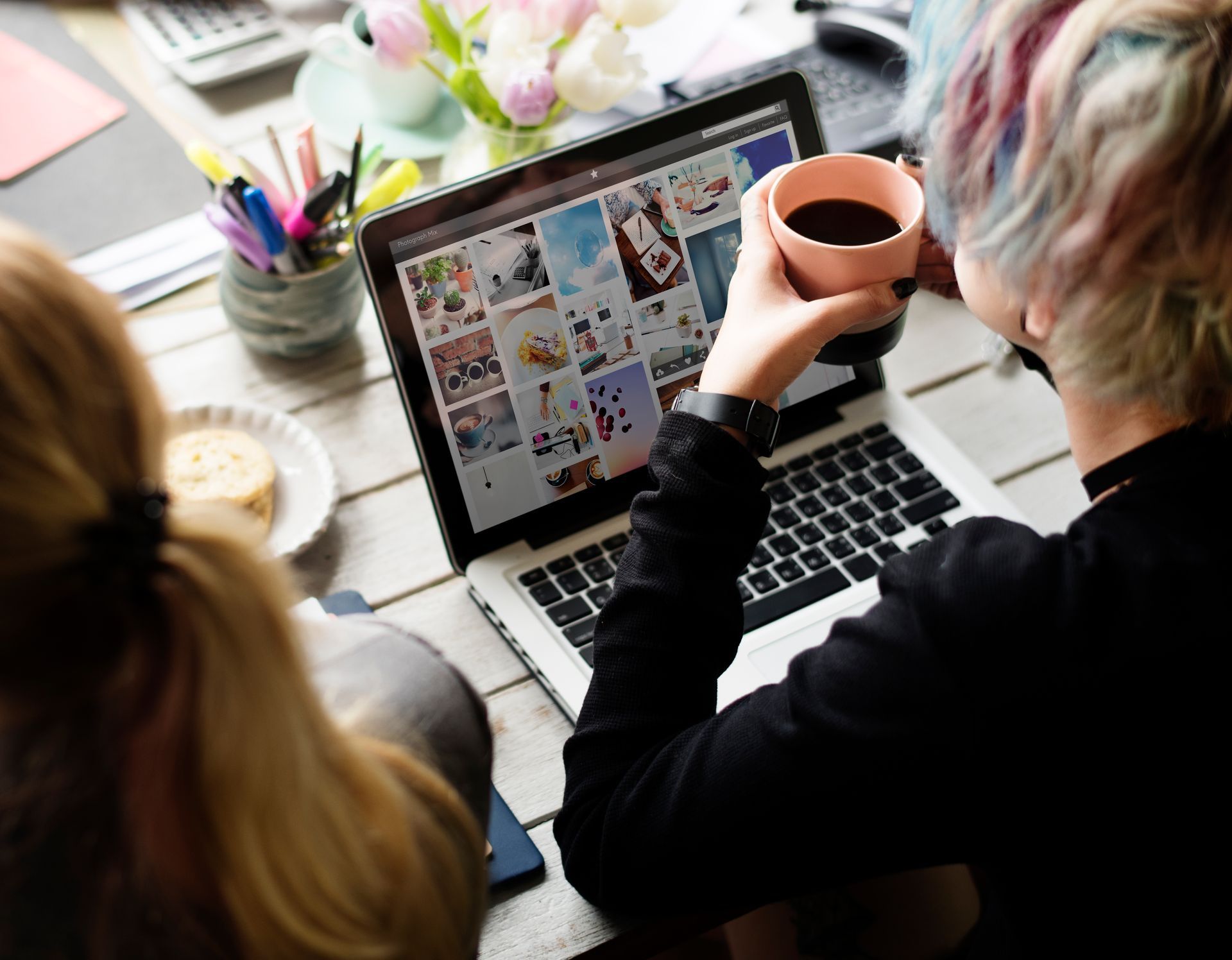 Una mujer sostiene una taza de café mientras mira una computadora portátil.