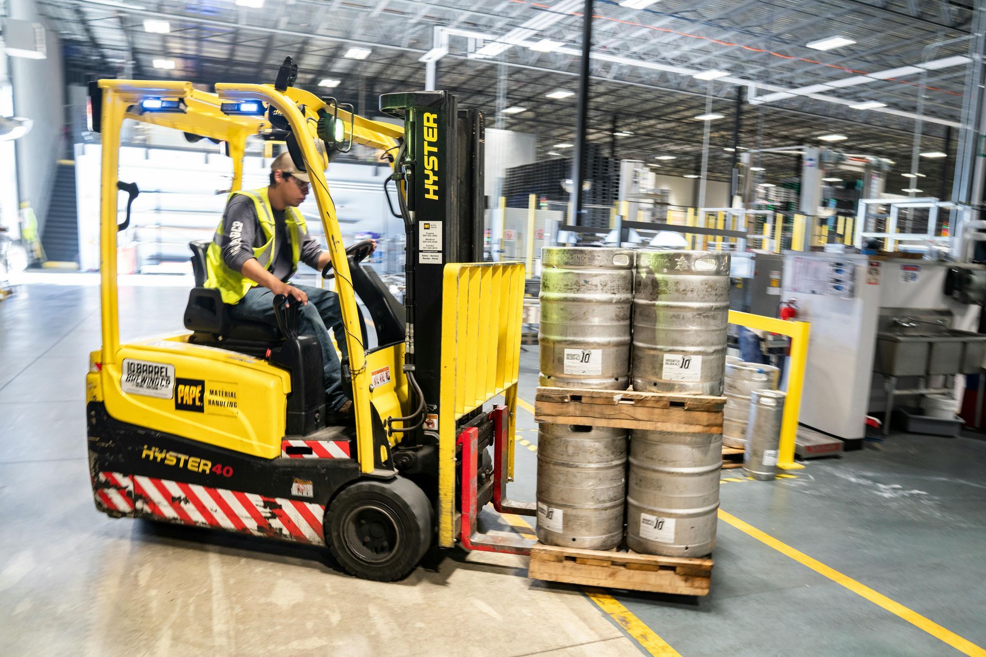 A man is driving a forklift in a warehouse filled with kegs.
