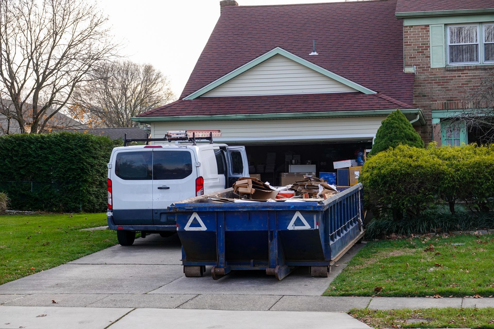 Pile of trash, black bags, furniture, debris on grass verge, residential neighborhood.