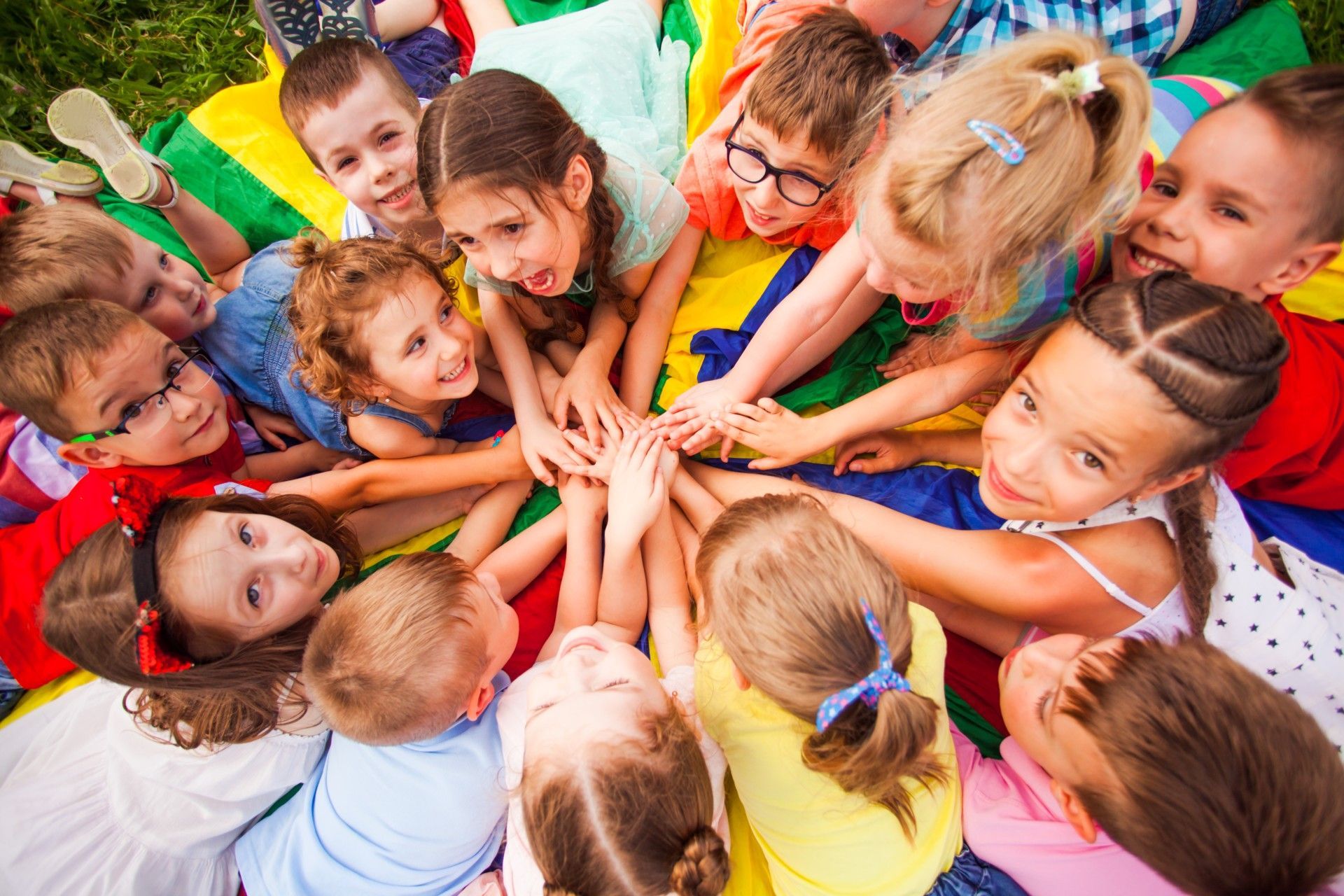 A group of children are laying in a circle on a parachute.