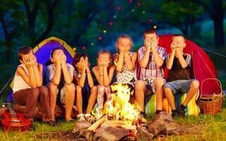 A group of children are sitting around a campfire in front of a tent.