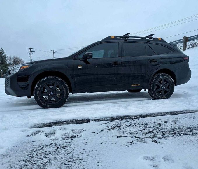 Black SUV parked on a snowy road with roof racks, viewed from the side.