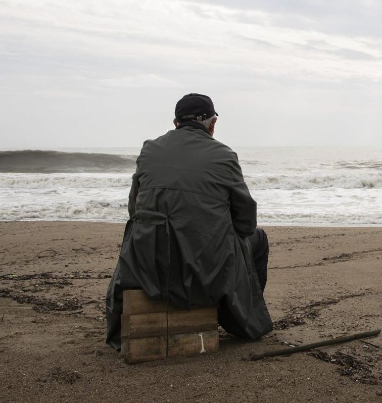 A man sits on a wooden box on the beach looking at the ocean