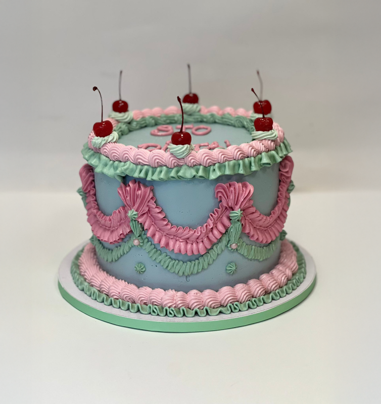 Torta decorata in blu e rosa con ciliegie sopra.