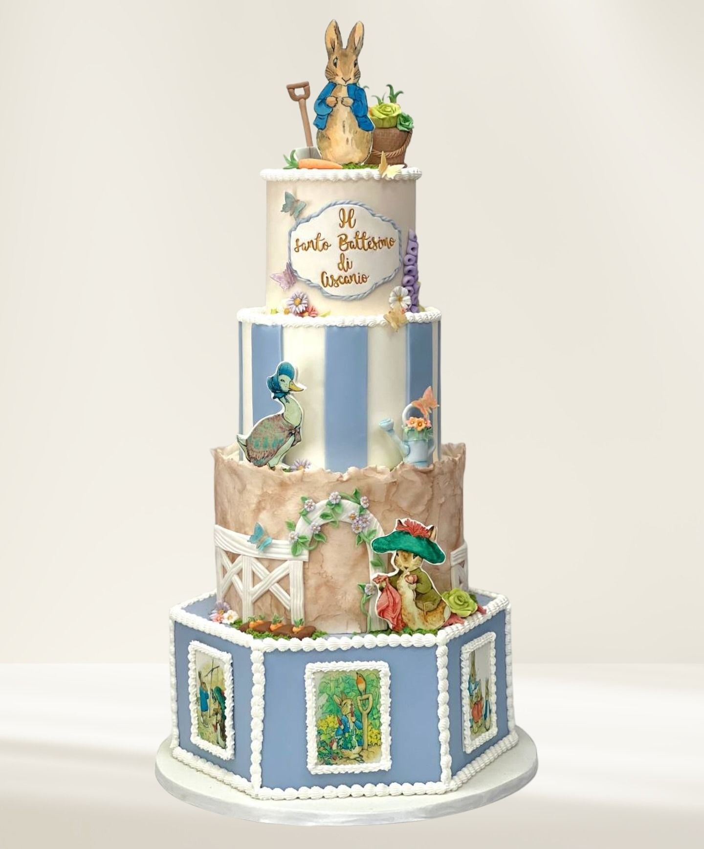 Torta a quattro piani a tema Peter Rabbit con strisce blu e bianche, illustrazioni e statuine.