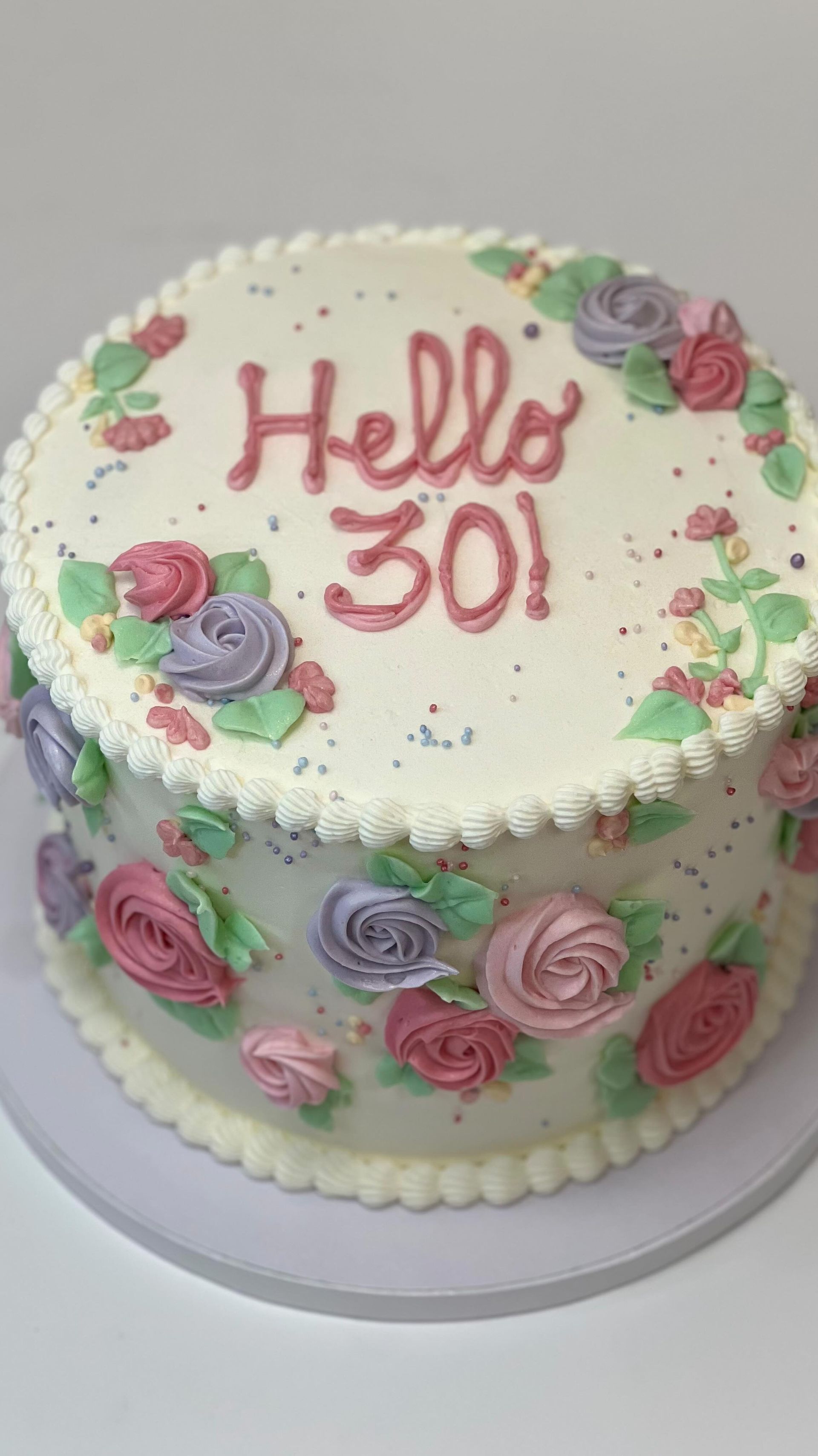 Torta decorata con glassa floreale rosa e viola, con la scritta