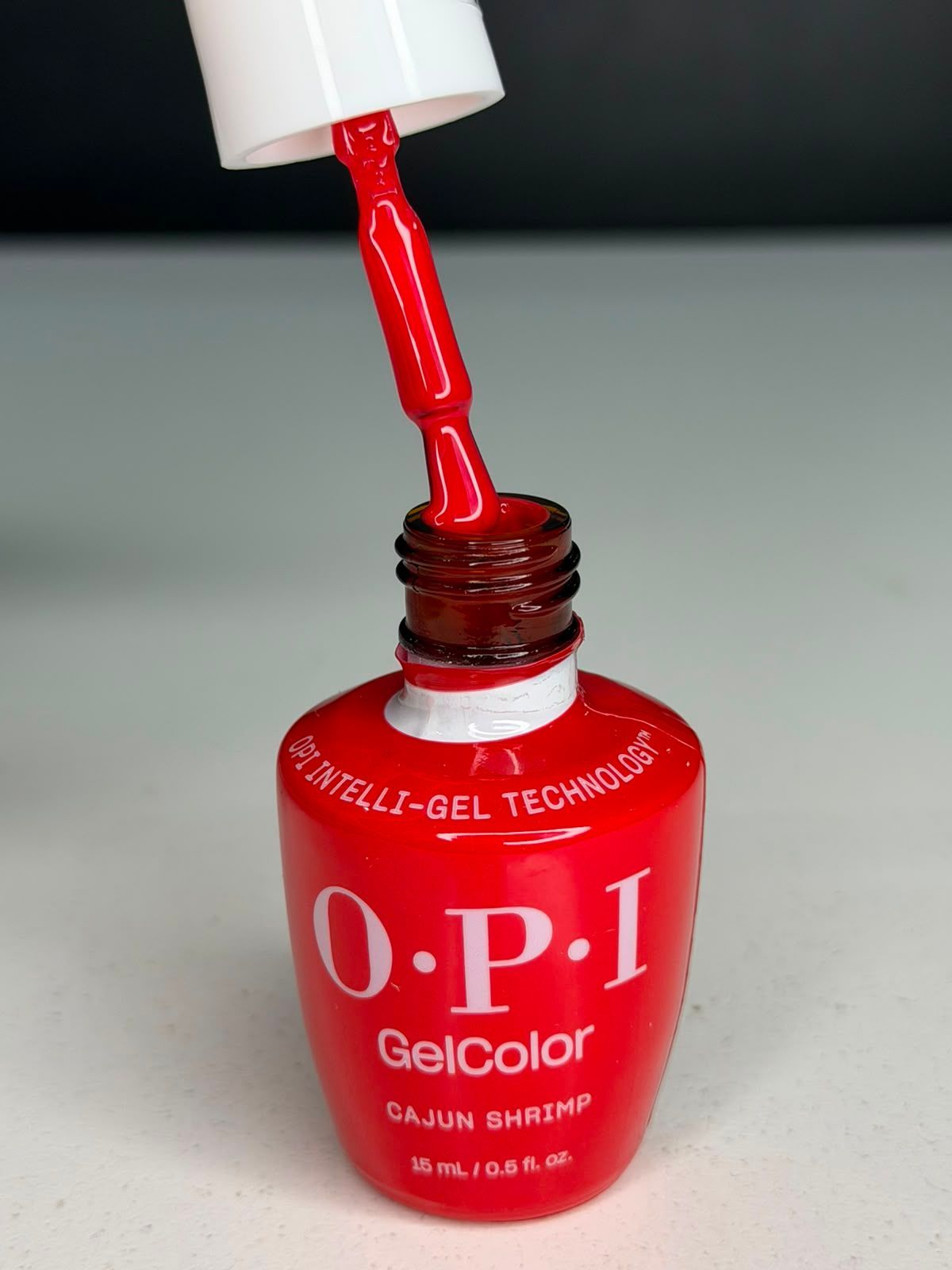Frasco de esmalte de uñas OPI GelColor rojo con tapa blanca y pincel al descubierto, mostrando el esmalte rojo goteando.