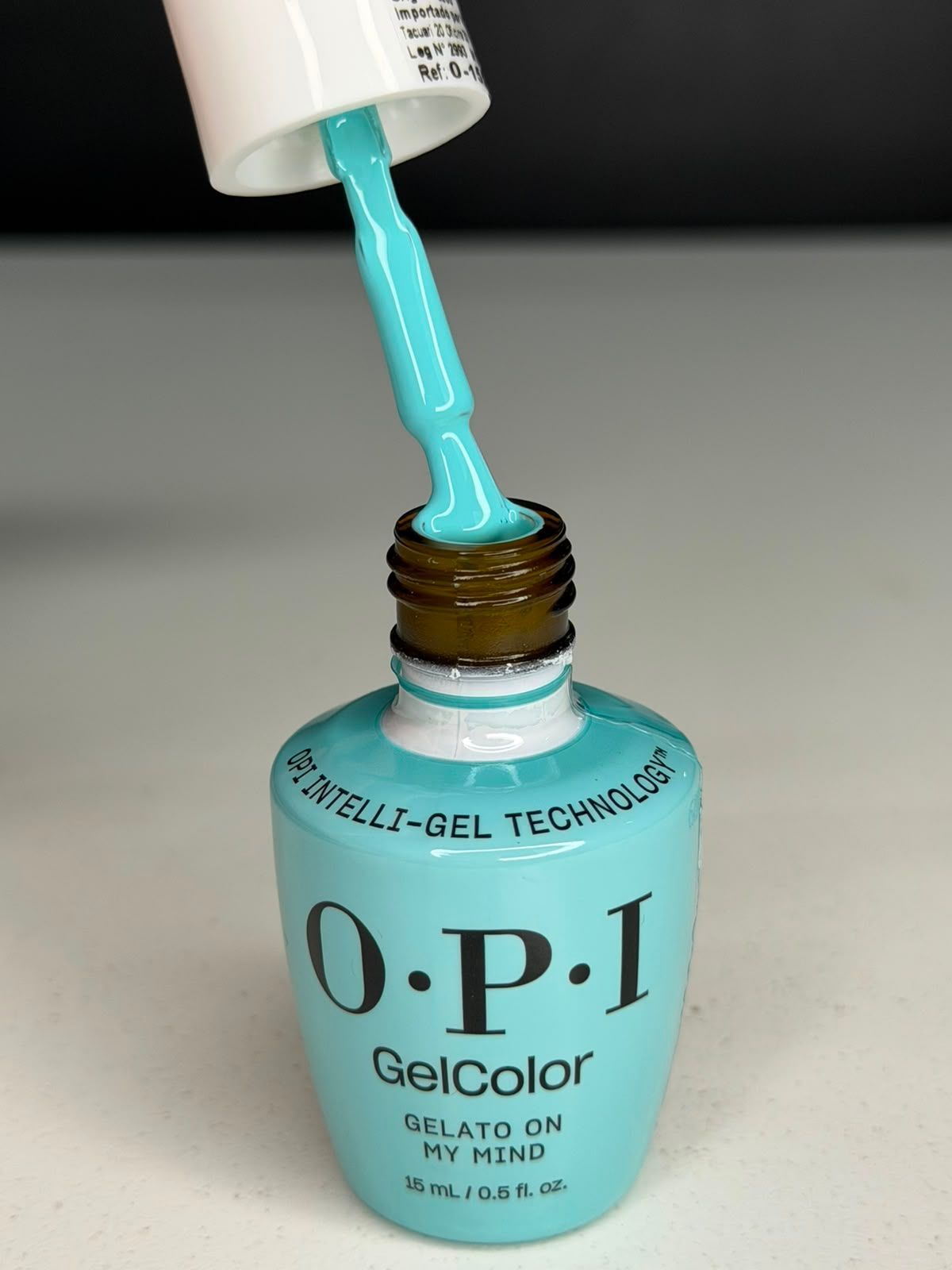 Frasco de esmalte de uñas OPI color turquesa con esmalte azul vertiéndose en su interior.