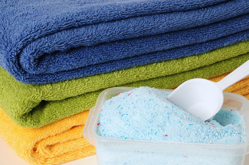 Stack of Towels Next to a Container of Blue Laundry Detergent — Flynns Beach Service Laundry in Lake Cathie, NSW