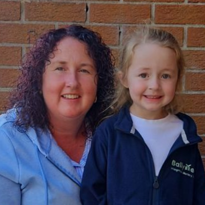 Woman with curly hair and child in front of a brick wall smiling, both looking at the camera.