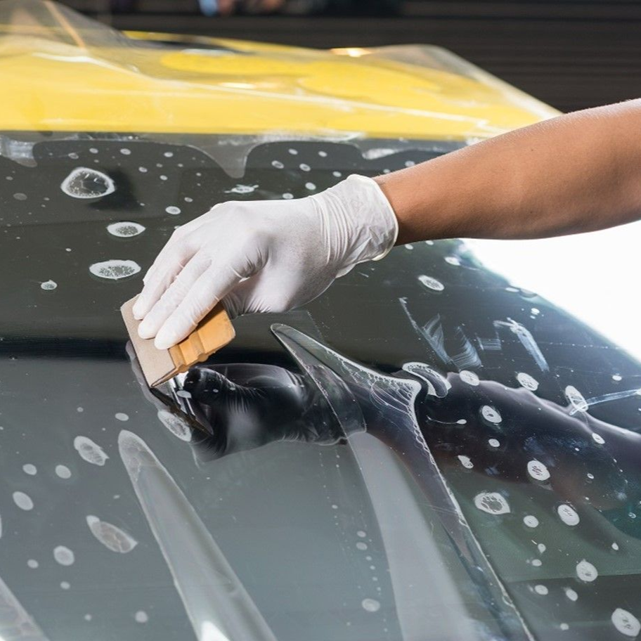 Person in gloves squeegeeing window tint onto car window. Bubbles of water are visible.
