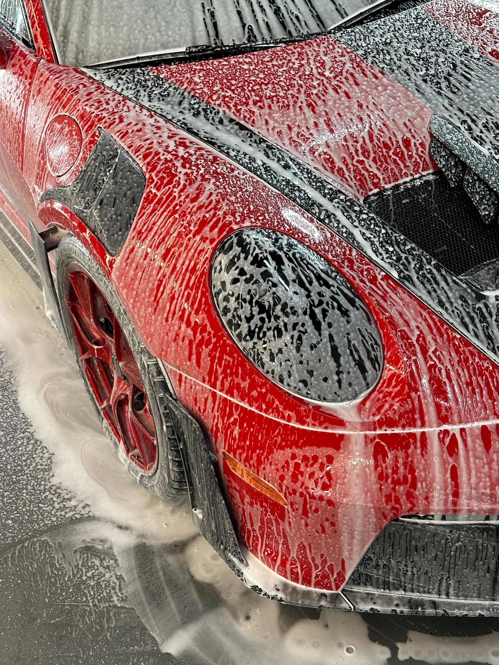 Red BMW M4 sports car parked near a garage in the rain.