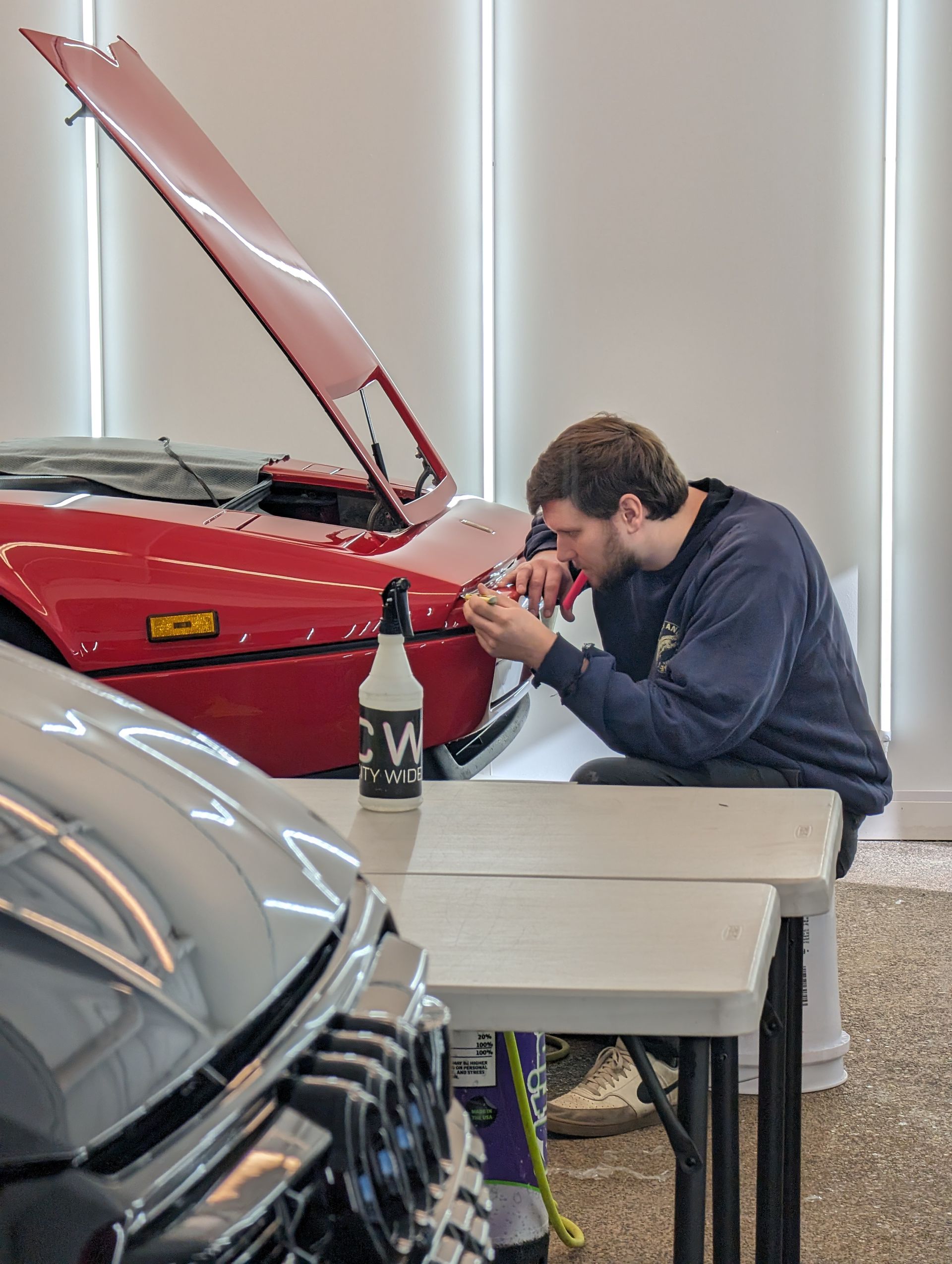A person applying clear protective film to a black car's headlight, using a squeegee.