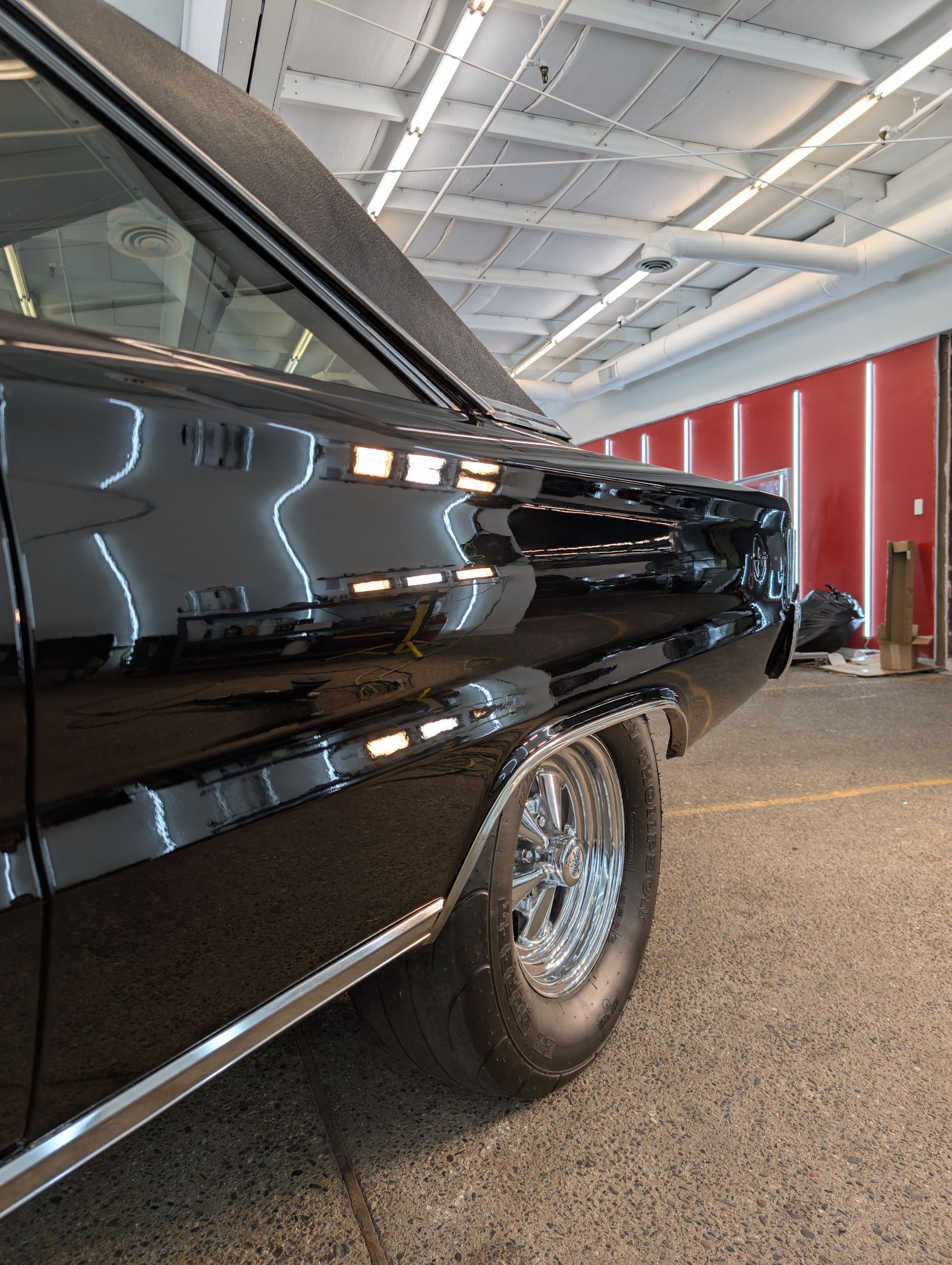 Black classic car in a brightly lit garage, showcasing its shiny paint and chrome wheel.
