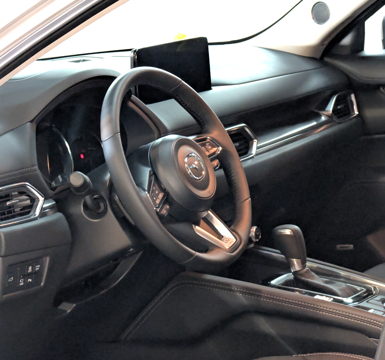 Interior view of a black Mazda CX-5, focusing on the steering wheel, dashboard, and gear shift.