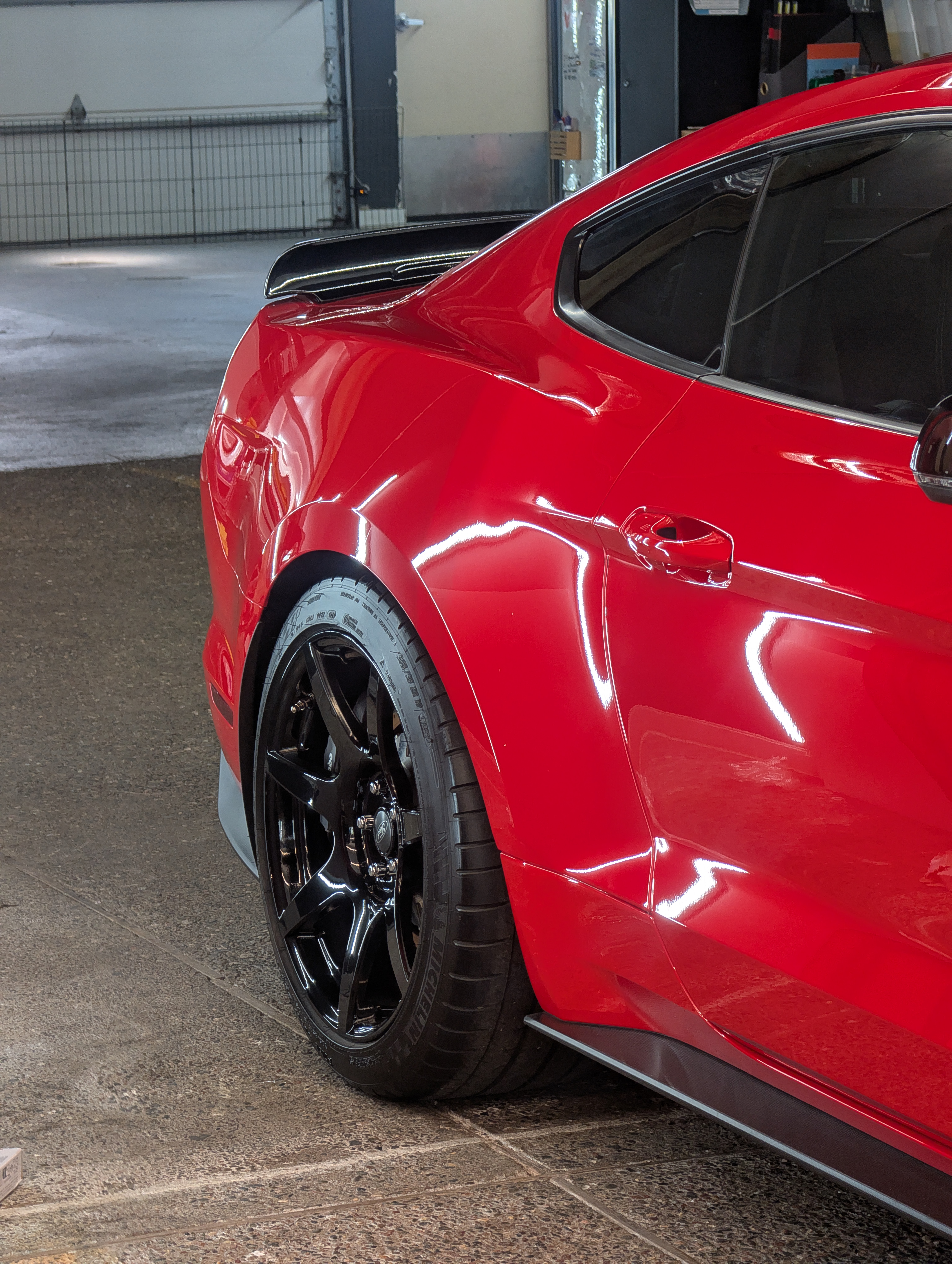 Red sports car with black rims, parked in a garage.