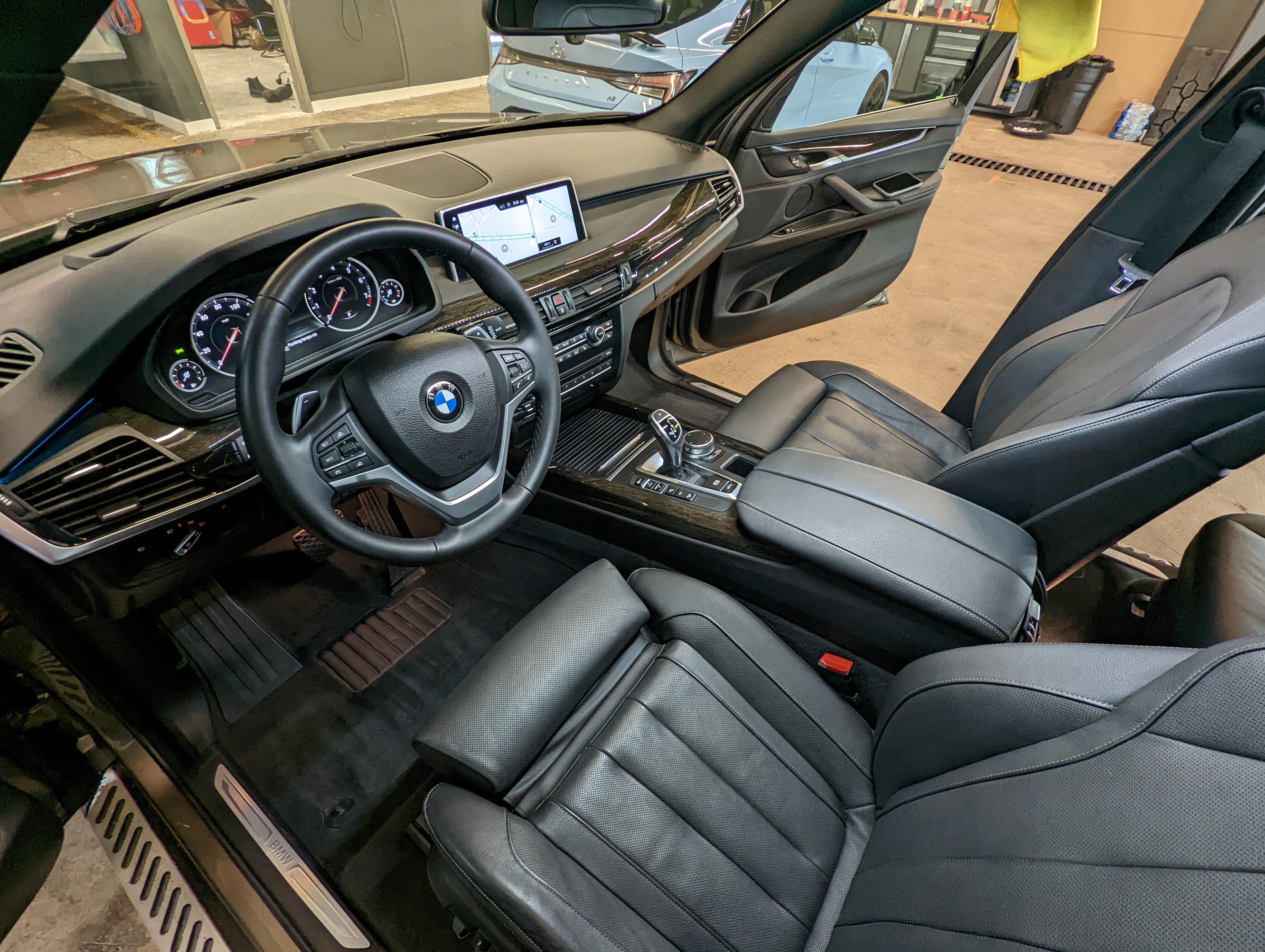 Interior view of a black BMW car with leather seats, steering wheel, and dashboard. Driver's side door is open.