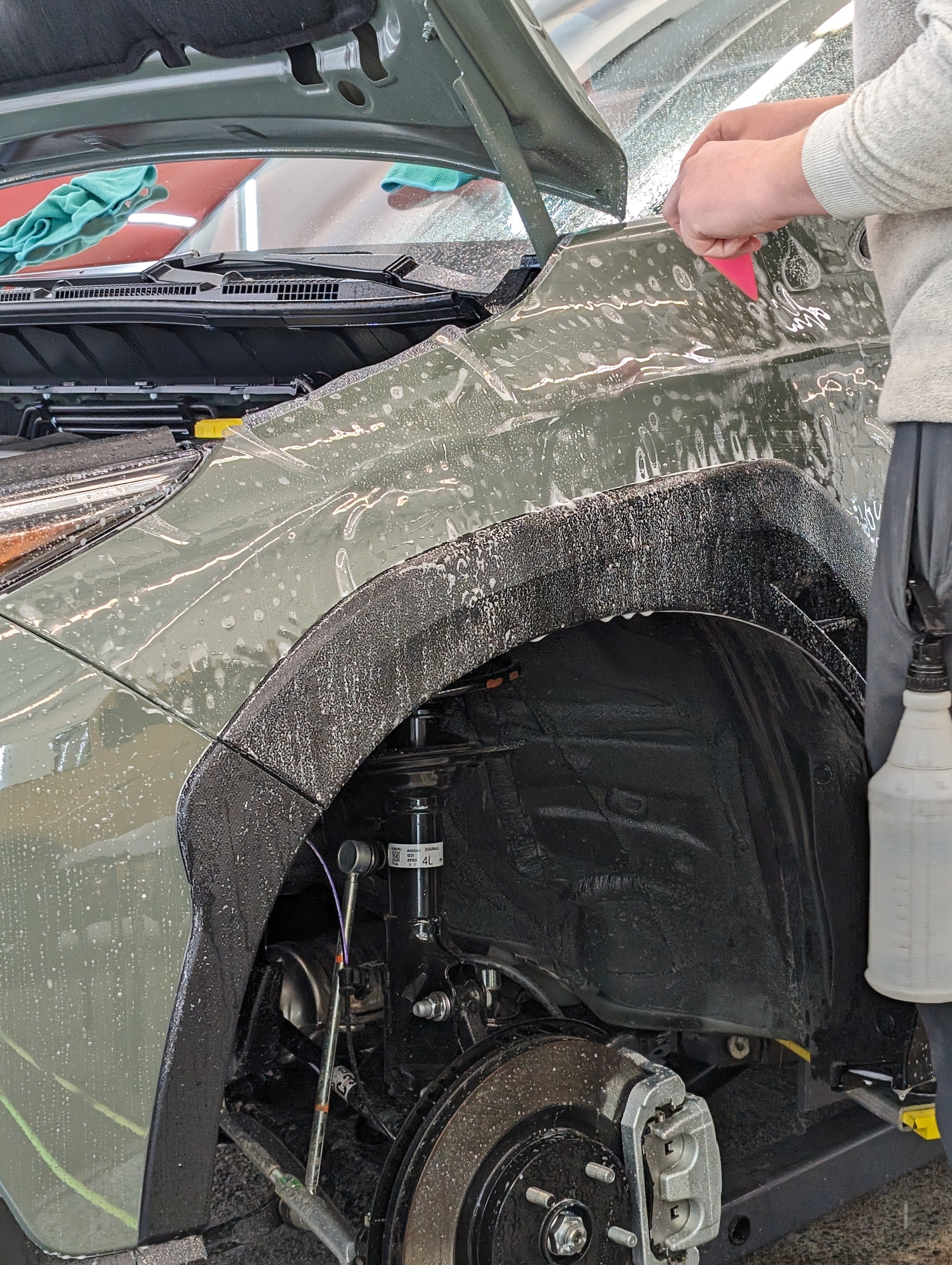 Person applying protective film to a green car fender with a squeegee.