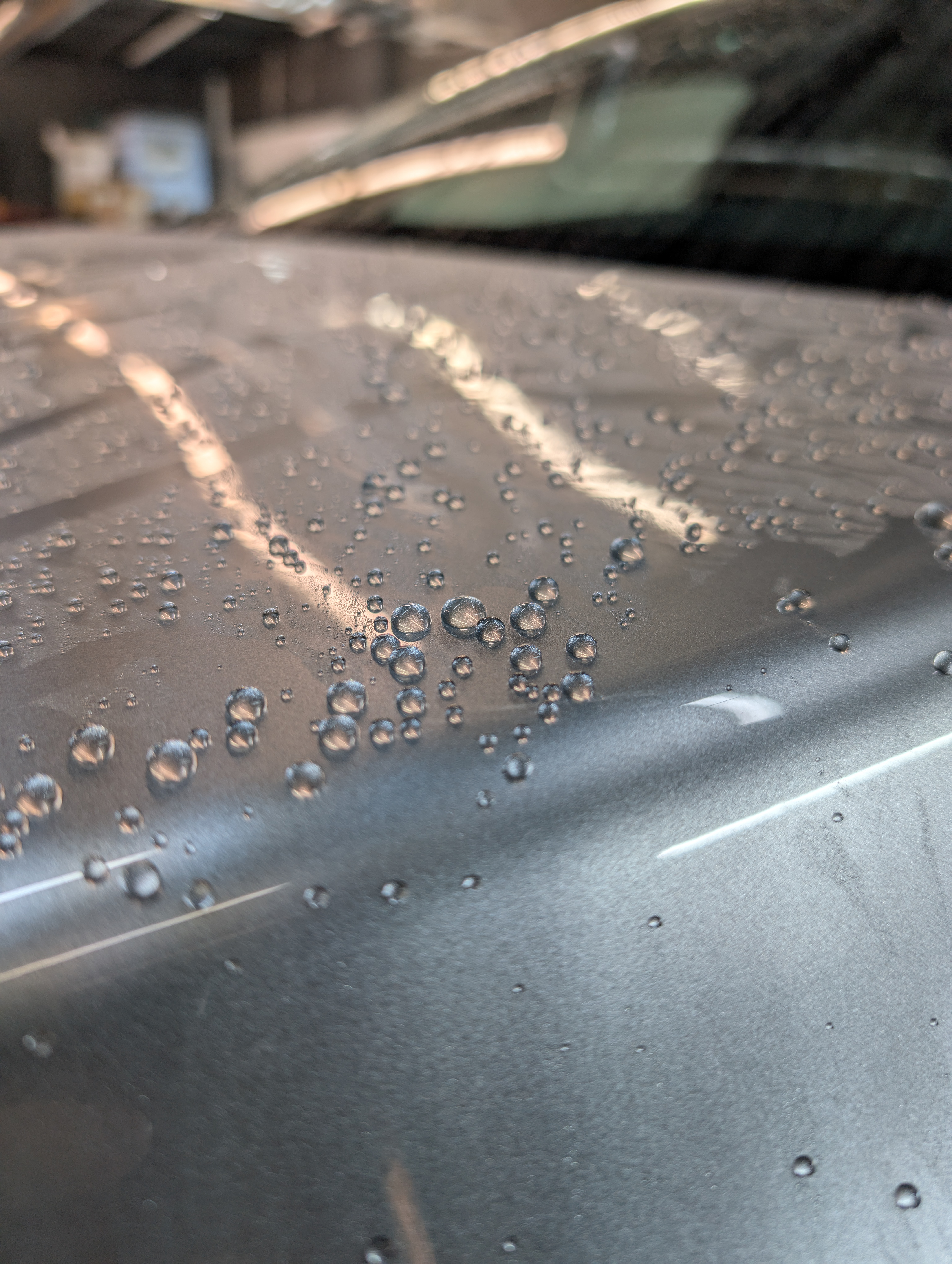 Close-up of a silver car hood with water droplets.
